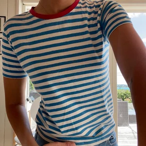 Blåvit randig t-shirt med röd krage strl S - Säljer denna t-shirt från okänt märke och utan angiven strl, men skulle gissa på S. Använt en del men är i bra skick. Köparen står för frakt!