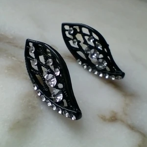 Oanvända svarta örhängen i metall med "diamanter" - Oanvända svarta örhängen i metall med "diamanter". 2.5 cm långa. Fraktpris 15 kr.