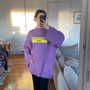 Lila stickad tröja/klänning - Lång stickad tröja (jag är 170cm lång normal stl S) lila med texten ”WOMEN OF THE WORLD UNITE” skick på materialet: använd men inga lösa sömmar eller hål. Vida ärmar. Brukar bära denna med bälte i midjan.