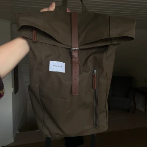 Sandqvist Dante Olive Ryggsäck - Jättefin ryggsäck från Sandqvist! Väldigt sparsamt använd — endast fått lite märken på framsidan (som bara ger en fin Vintage-look). Perfekt till skola el. arbete. Får plats med hur mycket som helst men ser fortfarande nätt och proper ut! Olivgrön/brun.