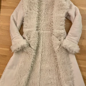 En benvit päls - En varm och härlig vadlång päls ( oäkta ) Två fickor, fyra knappar, insvängd i midjan. 
