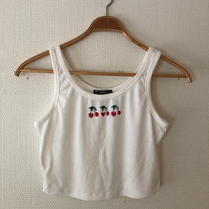 Vitt linne med tryck - Vitt ribbat croppat linne med körabärstryck från Shein. Storlek L men skulle säga att den är liten i storleken och kanske är mer som strl M (det får ni avgöra själva). Tunt material och lite genomskinlig. Nyskick. Tveka inte att skicka privat vid någon fundering eller om du vill ha någon mer bild på plagget!!🤍