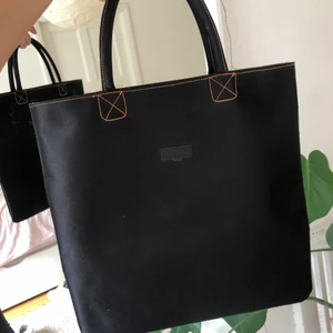 Lancome väska  - En väska i svart glansigt tyg med oranga sömmar från lancome. Perfekt storlek för datorn, har ett innerfack och handtagen är hårda och formade. Skriv för fler bilder eller vid frågor! 