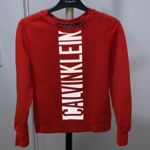Calvin Klein tröja  - Röd Calvin Klein tröja i storlek XS. Väldigt fin och unik. Texten ser ut som första bilden om man tar bild med flash och i vissa belysningar, annars är den svart så som på andra bilden. Tröjan är i väldigt bra skick, använd endast enstaka gånger. Tröjan är röd som på bild nr 1. 
