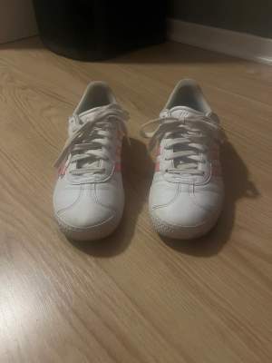 Ett par vita Adidas skor med ljus rosa ränder använda 10 gånger ksk dom e ass fina men dom e tyvärr jätte små för mig 💖jätte fin skick