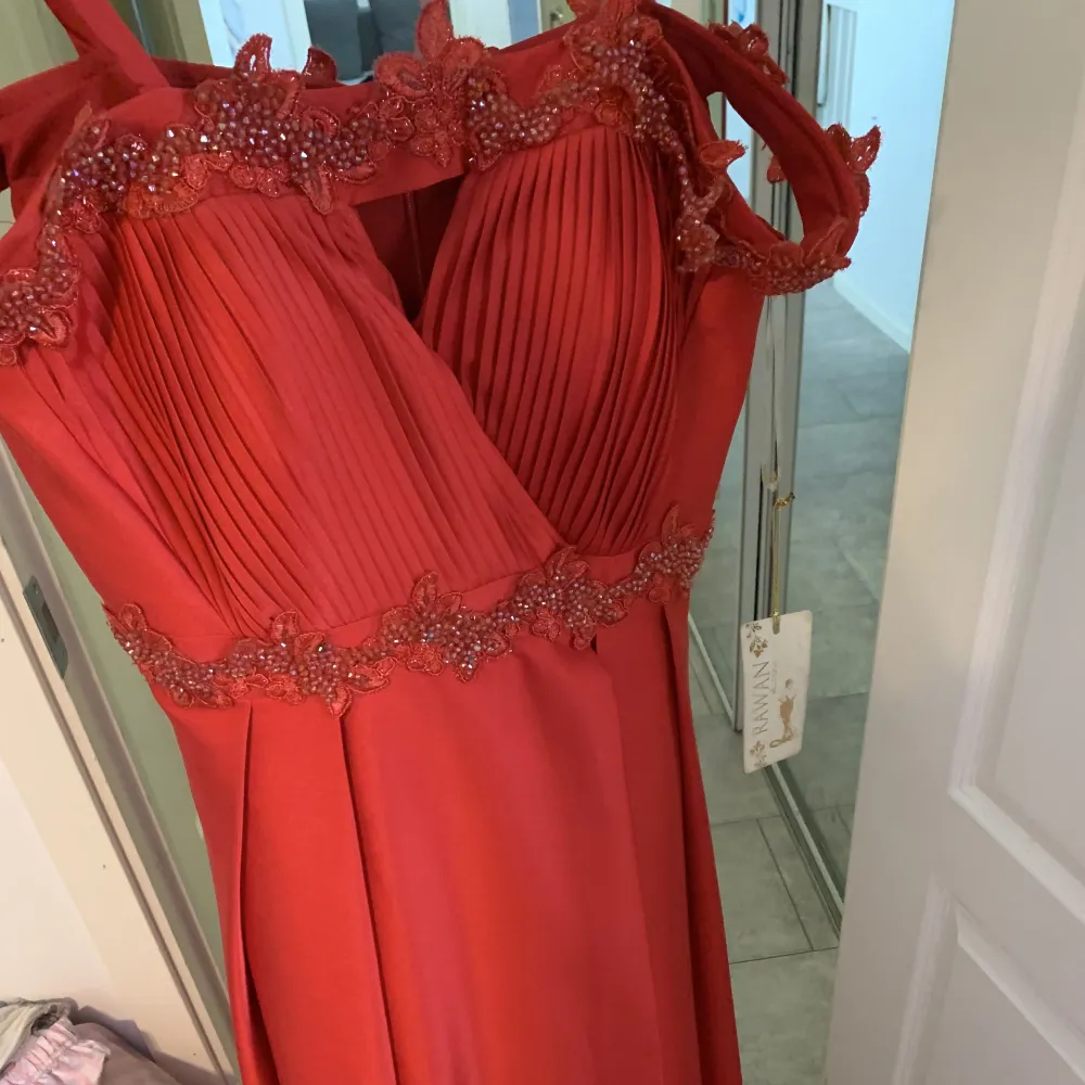 En helt ny klänning som inte har använts en enda gång, då klänning var liten och inte kunde lämnas tillbaka till butiken. Det är en lång röd klänning med slits som man kan ha till bröllop, bal även andra festliga tillfällen. . Klänningar.