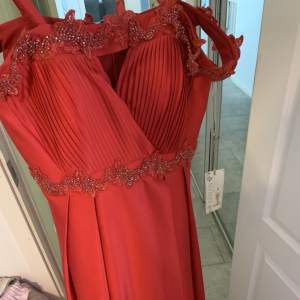 En helt ny klänning som inte har använts en enda gång, då klänning var liten och inte kunde lämnas tillbaka till butiken. Det är en lång röd klänning med slits som man kan ha till bröllop, bal även andra festliga tillfällen. 
