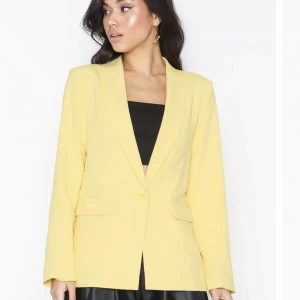 Gul blazer - En blazer från Nelly i denna härliga o så passande gula färg till våren! Helt oanvänd så sprillans ny i strl 34. Rak modell i vävd kvalité o stängs med en knapp framtill. Kavajen har  fickor med lock, vadderade axlar och fodrad. Köpt för 499kr