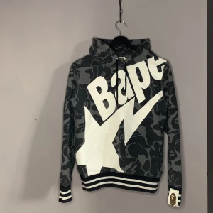 Bape hoodie - Bape hoodie grå/svart kamouflage med vit text nytt skick                                                                   Säljer min bape för att den är för liten                                                                           Storlek S