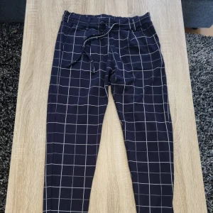 Rutiga långbyxor - Rutiga mörkblå byxor i mjukt material. Fikor fram, fejkfickor back och resår i midjan. Minns ej varifrån de kommer. Fint skick och knappt använda. Säljes pga garderobsrensning. 