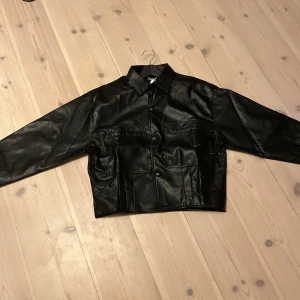 Läderjacka - Helt ny läderjacka med en cropped fit. Unisex, är storlek L men extremt liten i storlek, passar en XS/S herr. Aldrig använd med tags kvar på jackan. Är 100% veganskt läder, paketeringen finns kvar. Köpt för 1600kr