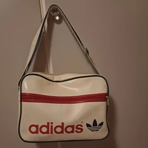Väska - Säljer denna axelremsväska från Intersport med märket adidas för 199kr. Urprungspris 499 kr. Bra skick, men för att se väldigt ny ut behövs tvätt.   Rik på förvaring. Justerbar. Ger 2000-2010 vibbar. (Köpt 2010, 11 eller 12)
