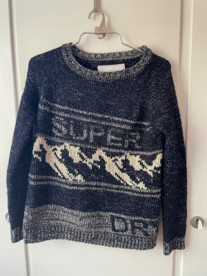 Superdry stickad tröja - Jätte fin stickad tröja från super dry. Mörkblå, vit, svart och silver färgad med glitter i mitten. Väldigt omhändertagen och bra skick