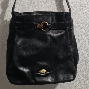 Väska The Bridge - Större handväska The Bridge i svart skinn. Mycket fint skick. Bredd 26, djup 14 och höjd 29 cm. Justerbar axelrem ca 95 cm.