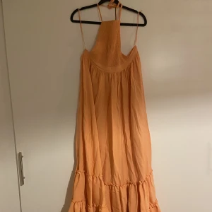 Långklänning  - Jätte fin långklänning med band i ryggen från Chiquelle. Storlek 38, men ganska liten runt bröstkorgen. Korall orange färg. Aldrig använd, endast testad. Köpt för 800:- Några små slitningar på den, se bilder. 