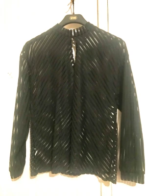 Svart transparent blus stl S/36 - Elegant blus med öppning fram och en knapp i nacken. Skönt material. Längd axel till fåll 66cm.