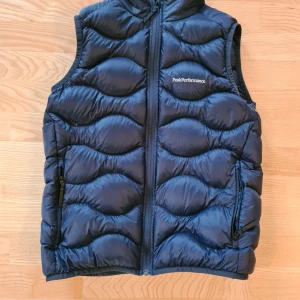 Peak Performance JR Helium Down Vest - Peak Performance JR Helium Down Vest, strl 160 eller XS. Använt sparsamt och köpt på KidsBrandStore hösten 2020. Passar till både sommar och mittersta höst då den är luftig men samtidigt isolerande för värme.