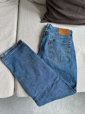 Blå Levi's raka jeans - Klassiska blå jeans från Levi's med rak passform och femficksmodell. Jeansen har en brun läderpatch bak i midjan och den ikoniska röda Levi's-taggen på bakfickan. Tillverkade i slitstark denim med dragkedjegylf och kontrastsömmar.