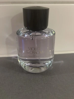 Violet Blossom parfym från Zara - Violet Blossom parfym från Zara Night Collection. Flaskan är rund och genomskinlig med lila toner och har en svart, stilren kork. Perfekt för dig som gillar blommiga och fräscha dofter. Snygg och modern design som passar på hyllan.