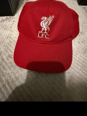 Röd Liverpool keps från '47 Brand - Snygg röd keps med Liverpool FC:s klassiska logga broderad framtill. Kepsen är från '47 Brand och har böjd skärm samt justerbar passform. Perfekt för dig som vill visa ditt stöd för LFC med stil.