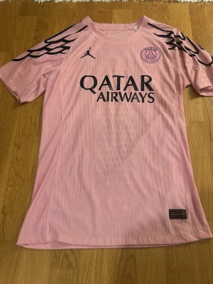 PSG rosa matchtröja med tryck - Säljer en rosa Paris Saint-Germain matchtröja från Jordan med svarta detaljer, vingmönster på axlarna och tryck 'Qatar Airways' på bröstet. Nummer 47 och namnet 'Sorcière' på ryggen. Tillverkad i lätt funktionsmaterial.