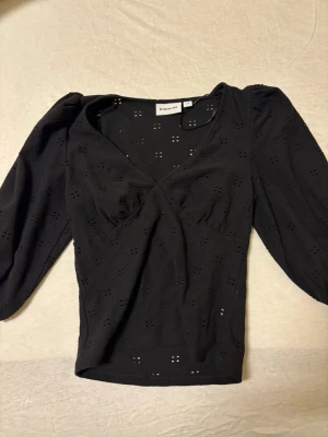Svart blus med puffärm från KappAhl - Snygg svart blus från KappAhl med v-ringning och puffiga långärmar. Blusen har broderade hålmönster över hela tyget och en lätt omlott-effekt framtill. Har bara använt den typ 2 gånger. 