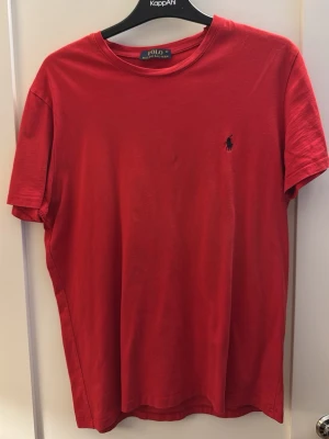 Röd t-shirt från Polo Ralph Lauren - Klassisk röd t-shirt från Polo Ralph Lauren med rund halsringning och korta ärmar. T-shirten har den ikoniska lilla broderade loggan på bröstet och är tillverkad i mjuk bomull för en skön känsla. Perfekt till jeans eller shorts.