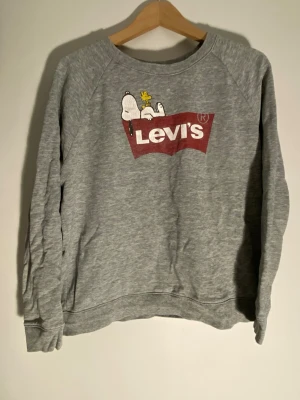Levis x Peanuts Snoopy tröja - Säljer en grå sweatshirt från Levi’s populära Snobben-samarbete. Trycket har börjat släppa på vissa ställen, vilket ger tröjan en skön vintage-look. Storlek M 