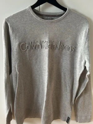 Grå sweatshirt från Calvin Klein Jeans - Snygg grå sweatshirt från Calvin Klein Jeans med broderad logga framtill. Tröjan har rund halsringning, långa ärmar och ribbade muddar vid ärmslut och nederkant. Perfekt för en clean och stilren look.