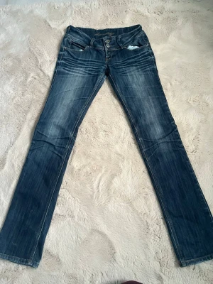 Mörkblå slim fit jeans med slitningar - Snygga mörkblå slim fit jeans med slitningar och ljusa tvättade detaljer. Jeansen har dubbla knappar i midjan, klassiska fem fickor och dekorativa sömmar på bakfickorna. Perfekta för en trendig och avslappnad look. Ett hål baktill under men enkelt att fixa. Jag köpte de så