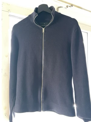 Mörkblå stickad ziptröja - Snygg mörkblå stickad tröja med dragkedja framtill och hög krage. Tröjan har en enkel, stilren design och är perfekt för lager-på-lager. Långa ärmar och mjukt material gör den både bekväm och lätt att matcha.