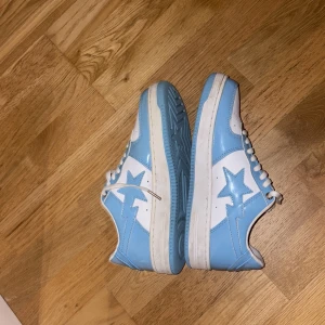 BAPE STA sneakers blå och vita - Säljer ett par BAPE STA sneakers i blått och vitt med klassisk stjärndesign på sidan. Skorna har snörning, perforerad tå och platt sula. Tillverkade i glansigt syntetmaterial som ger en clean och fräsch look. Perfekta för dig som vill sticka ut med streetwear. Och pris kan diskuteras 