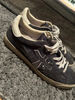 Premiata blåa sneakers i mocka - Snygga blåa sneakers från Premiata i mocka med vita detaljer och vita skosnören. Klassisk låg modell med logga på sidan och kontrasterande vit häl. Perfekta för en clean och stilren look.