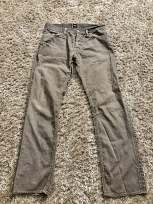 Grå jeans från BOSS Hugo Boss - Säljer ett par grå jeans från BOSS Hugo Boss med klassisk femficksmodell och raka ben. Jeansen har silverfärgade nitar och bälteshällor. Materialet är denim i bomull med en snygg tvättad look. Jag har ärvt de från en vän och det står tyvärr ingen storlek men jag har testat de och jag skulle säga att de är i storleken 30/32, 30/33Perfekta för en avslappnad och stilren outfit och är riktigt sköna. Har du några frågor så är det bara att skriva🙌
