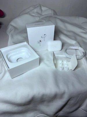 Apple AirPods Pro med laddningsetui - Säljer ett par vita Apple AirPods Pro med trådlöst laddningsetui. Inkluderar originalförpackning, extra silikontoppar och laddningskabel. Snygg och stilren design i plast, perfekt för dig som vill ha grymt ljud och smidig anslutning till iPhone eller andra Apple-enheter.