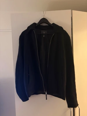 Svart jacka från H&M - Stilren svart jacka från H&M med dragkedja framtill och klassisk krage. Tillverkad i ullblandning med slät insida och raka ärmar. Perfekt för dig som gillar minimalistisk och tidlös design.