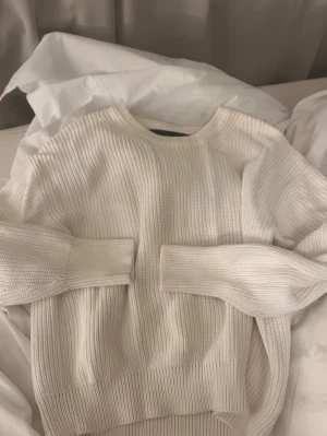 Vit ribbstickad tröja  - Säljer en stilren vit ribbstickad tröja. Tröjan har rund halsringning, långa ärmar och breda muddar vid ärmslut och nederkant. Perfekt för lager på lager och enkel att matcha med olika outfits.