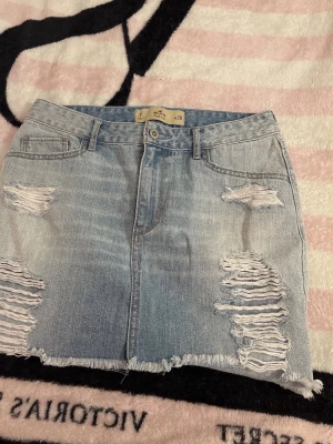 jeanskjol från Hollister - Ljusblå  jeanskjol från Hollister med slitna detaljer och fransad nederkant. Klassisk femficksmodell med dragkedja och knapp framtill. Perfekt för dig som gillar en avslappnad och trendig stil.