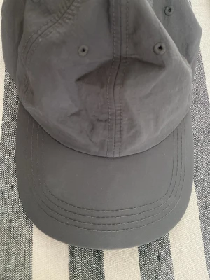 Mörkgrå keps från Carin Wester - Snygg mörkgrå keps från Carin Wester, modell LEAH. Tillverkad i ett lätt och slitstarkt material med böjd skärm och ventilerande öljetter. Perfekt accessoar för en avslappnad och trendig stil.