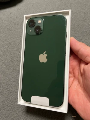 Grön iPhone 13 med dubbla kameror - Snygg grön iPhone 13 med stilren design och två bakre kameror. Baksidan är i glas och ramen i aluminium. Ikoniska Apple-loggan syns tydligt på baksidan. Perfekt för dig som vill ha en modern och kraftfull smartphone. a small dot in the right corner but its not affect any thing