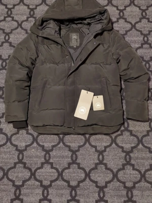 Svart pufferjacka med huva - Väldigt fin canada goose macmillian jacka i nyskick till salu. Bara att höra av sig vid funderingar:)
