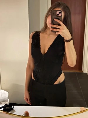 Svart spetsbody med djup urringning - Säljer en svart body i spets med djup v-ringning som går att reglera vid skulderbladen för att få en bättre personlig passform. Bodyn har fina spetsdetaljer och är skuren högt vid höfterna för en smickrande siluett.                                               Är storlek M men har vanligt vis xs/s. 