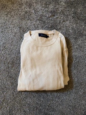 Beige tröja från Riley - Snygg beige tröja från Riley med rund halsringning och diskret struktur som är i materialet. Perfekt basplagg som är lätt att matcha med olika stilar. Tillverkad i mjukt tyg för en bekväm känsla hela dagen.