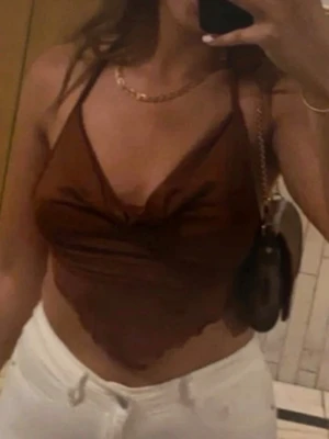 Brun halterneck topp med drapering - Säljer en brun halterneck topp med snygg drapering framtill och tunna axelband. Toppen har en croppad passform och är gjord i ett mjukt, stretchigt tyg som känns skönt mot huden. Perfekt för sommarens alla tillfällen!