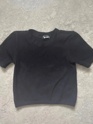 Svart cropped t-shirt S Zara - En enkel svart cropped t-shirt med rund hals och korta ärmar. T-shirten har en tight passform och är tillverkad i ett mjukt, stretchigt material. Perfekt för en avslappnad och trendig look.