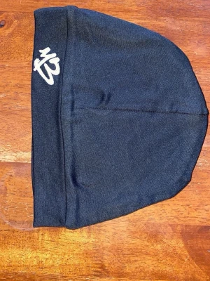 Svart mössa med M3-brodyr - Snygg svart mössa med vit M3-brodyr framtill. Tillverkad i ett tunt, stretchigt material som sitter skönt på huvudet. Perfekt för dig som vill ha en enkel och stilren accessoar till höst och vinter.