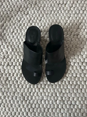 Svarta slip-in sandaler med klack - Stilrena svarta sandaler från & other stories i minimalistisk design. Slip-in modell med bred rem över foten och tårem, samt låg blockklack. Tillverkade i slätt läder som ger en modern och clean look. 