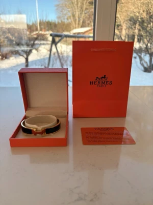 Svart armband med gulddetalj - Snyggt svart armband med ikonisk H-detalj i guld. Armbandet har en elegant och stilren design, tillverkat i läder och metall. Kommer i originalförpackning med tillhörande påse och certifikat.