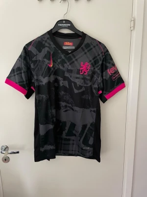 Svart och rosa Nike fotbollströja - Snygg svart fotbollströja från Nike med grått kamouflagemönster och rosa detaljer. Riktigt fet tröja till sommaren eller när som storlek L men passar som M