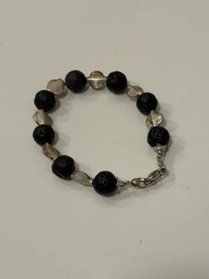 Armband med svarta lavastenar och silverdetaljer - Handgjort armband med svarta lavastenar och silvriga mellanpärlor. Armbandet har ett metallspänne som gör det enklare att ta på och av 